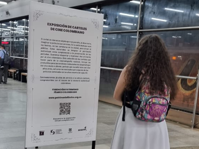 Exposición de carteles de cine colombiano en la estación Museo Nacional, usuaria viendo un cartel
