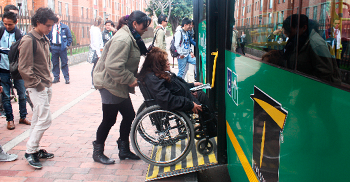 Persona ayudando a una persona en silla de rueda a subir por la plataforma  de un alimentador